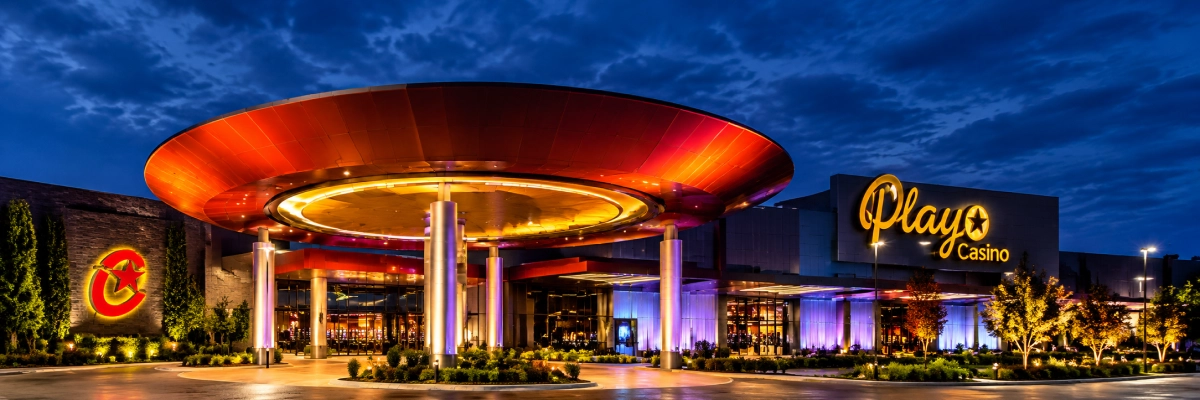 Exterior of a Playo Casino at night, illuminated by lights and surrounded by trees, plants, and poles